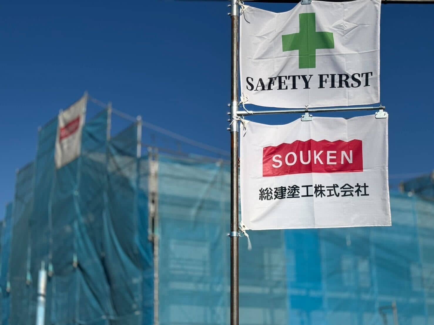 工事現場の安全旗と総建塗株式会社の社名旗が風になびいている様子